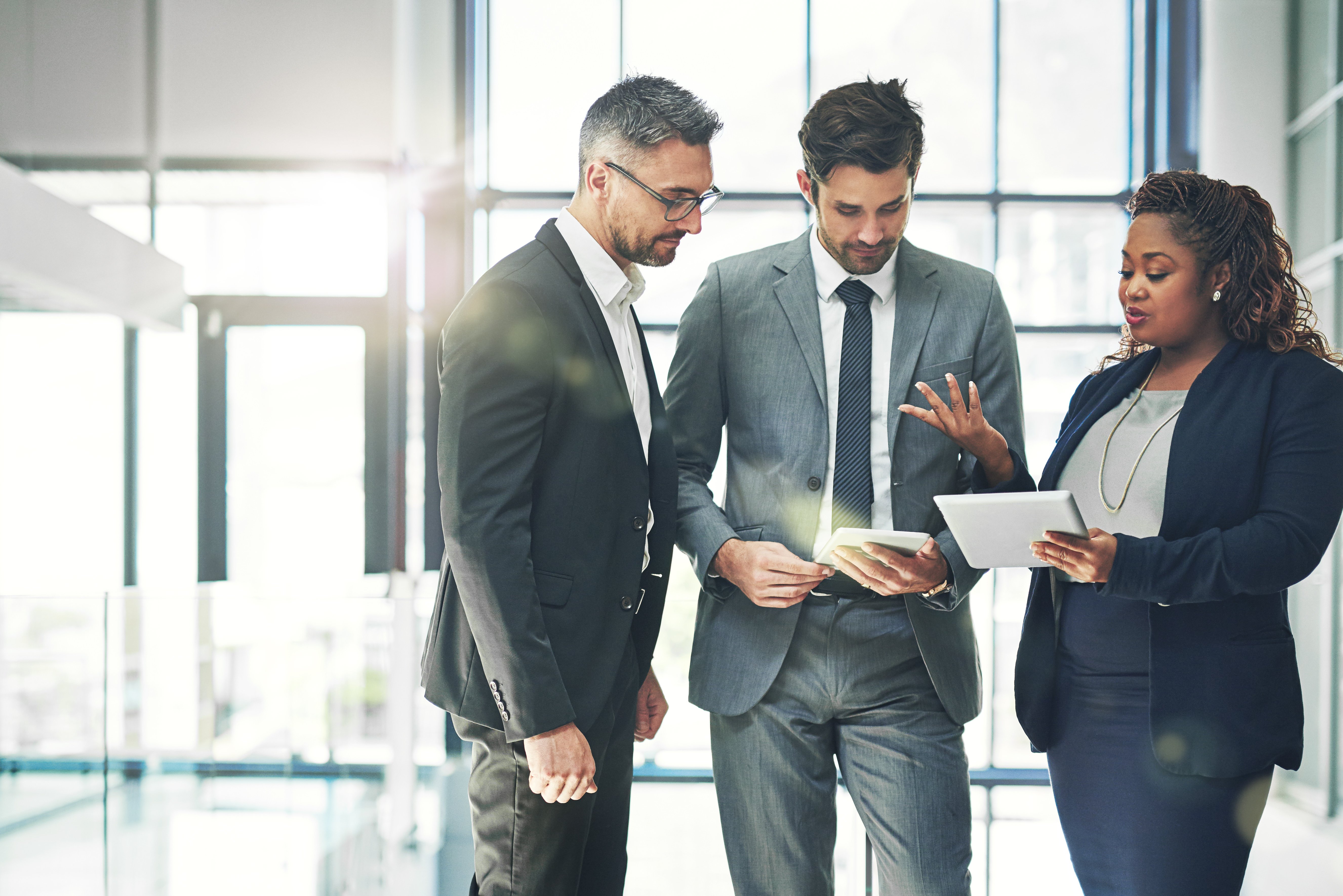 Two businessmen and a businesswoman looking through electronic documents on their tablets